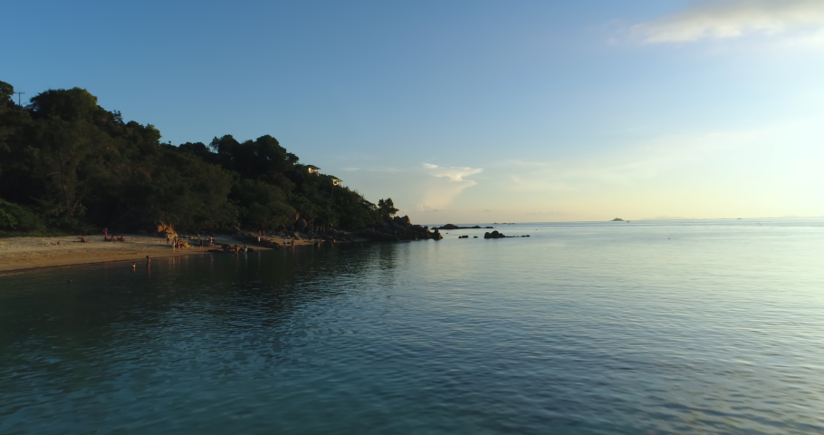 Hyperlapce Thailand island aerial: ocean coastal sandy beach with resting people. Tropic landscape: mountains with leafy trees and buildings under foliage. Green Thai jungle wildlife shot in 4K, UHD