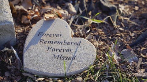 Slow Motion Close Up of Heart Shaped Grave Stone Saying Forever Remembered Forever Missed in Stone and Text on Grass and Ground