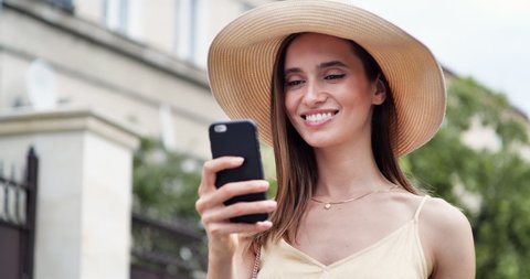 Caucasian young Woman with amazing Smile is using Smartphone, New Apps. Getting positive Emotions, having Fun while browsing Phone. Exited Woman testing New Apps, Social Networks, walking Outside.