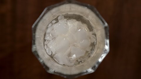 Slow motion shot of hand pouring soda liquid into glass with cold ice cubes inside bar.Top down.