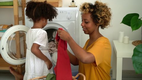 afro mom and daughter load washer with dirty clothes Spbd. mother and kid do housework with washing machine. child help mom with laundry and housework. concept domestic, american, bathroom