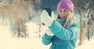 Woman traveler with her phone camera taking pictures beautiful winter snowy forest view. Happy winter holidays. New Year's Eve. Christmas holiday. 4K video Slow motion.
