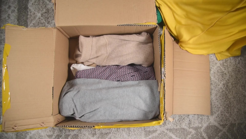 Clothes for donation packing in cardboard box. Top view of packing second hand clothes in parcel. Royalty-Free Stock Footage #1066060960