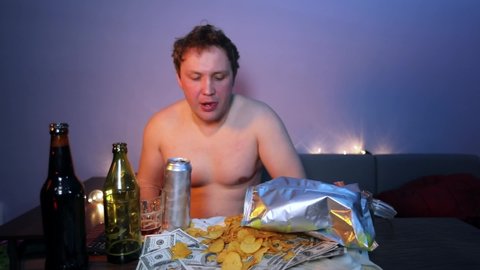 Boor man with a naked torso eats chips and drinks beer