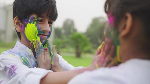 Close shot of smiling and cute little boy and girl applying powdered colors on each others face on the occasion of Indian festival Holi