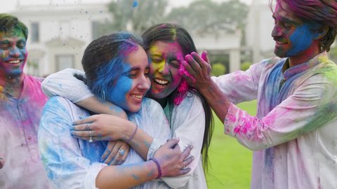 Young and affectionate male and  female friends are applying colors on face and hugging each other while celebrating holi outdoors. 