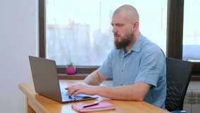 Male employee works at home office at the computer. Bearded businessman looking at laptop screen, working remotely at home. 