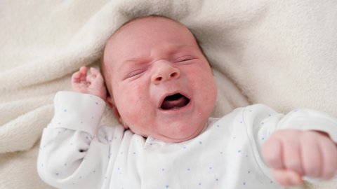 Closeup portrait of newborn baby crying and screaming while lying in crib.