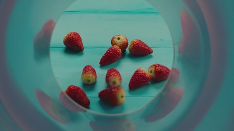 Many pieces of strawberries falling on green wooden table in slow motion. Camera view of inside package. Strawberries falling from package to green background. Shot on ARII camera with Laowa lens