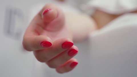 Woman lies on a hospital bed close-up. Palm of hand with red nails soft focus