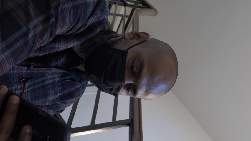 Adult Male Wearing Face Mask Checking Mobile Sitting Down On Stairwell. Locked Off, Vertical Video, Low Angle