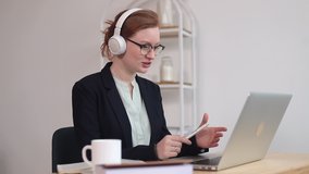 young caucasian woman in glasses and white headphones at home office holds a video conference with business partners, online negotiations, business online. Business woman at the laptop communicates