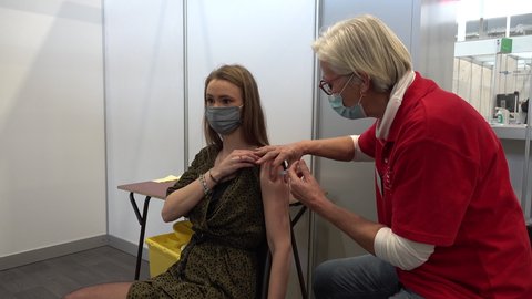 ROTTERDAM, NETHERLANDS – 21 JANUARY 2021: Young woman receives Pfizer BioNTech vaccine through syringe needle inside vaccination center. Europe begins Covid-19 coronavirus vaccination program.