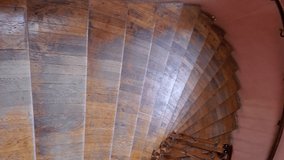 Walking down by old wooden spiral staircase with ornate railings and shabby parquet steps. Vertical format video of downstairs descent