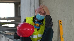 Slow Motion Builder in medical protective face mask sits on concrete floor of construction site. He is not feeling well and has a headache, he takes off hard hat and massages his head - Powered by Shutterstock - Get 15% off with code: PIKWIZARD15