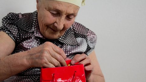 Old grandmother with a gift in her hands.Congratulations concept.International Women's Day. Happy grandmother with a smile examines a gift for Mother's Day.The old grandmother opens the gift. 