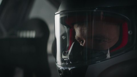 CU portrait of sports car driver closing helmet visor, starting a race on a speedway. Shot with 2x anamorphic lens