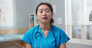 Charming female blogger with stethoscope in medical uniform making video. Young Asian nurse live streaming, talking to followers and speaking on camera in hospital. Internet, social media, medicine.