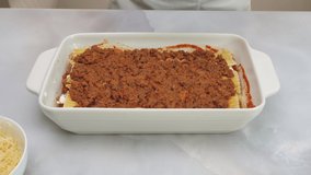 Beef lasagna step by step recipe. Topping lasagna with marinara sauce. Close up video, front view, woman hands, marble kitchen table background