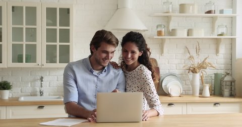 Bonding millennial smiling couple looking at laptop screen, choosing goods in online store involved in internet shopping, discussing planning vacation trip booking hotel or flight tickets on computer.