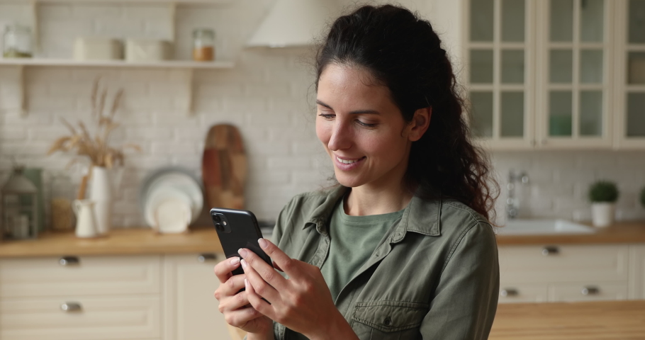 Smiling pretty young european appearance woman looking at smartphone screen, watching photos in online dating application or choosing goods services in internet store, shopping or communicating. Royalty-Free Stock Footage #1066095922