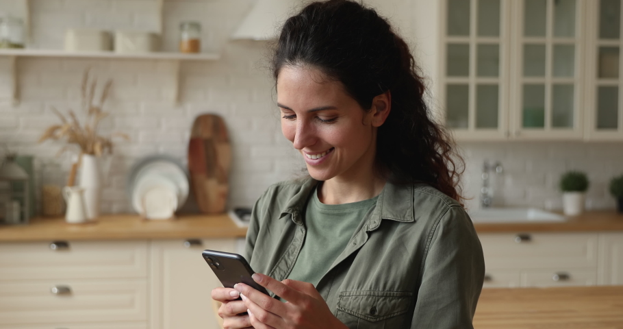 Smiling pretty young european appearance woman looking at smartphone screen, watching photos in online dating application or choosing goods services in internet store, shopping or communicating. | Shutterstock HD Video #1066095922