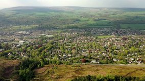 Ilkley aerial video. Flying over Ilkley Moor towards the West Yorkshire town, showing tree lined streets and residential houses from above, with green hills beyond.