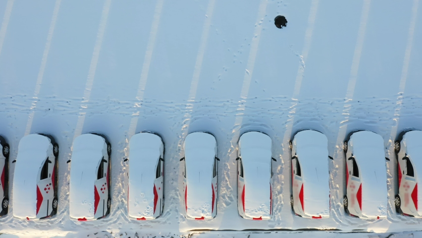 A row of delivery cars covered with snow stand in the parking lot of the logistics park on a winter day. Aerial top down view