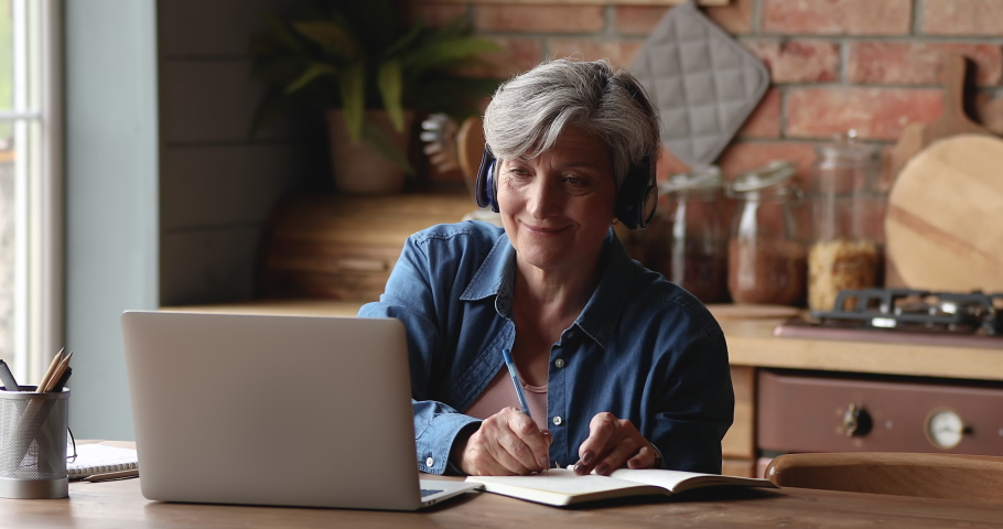 Older 60s woman search information writes it down on copybook, listen language audio course through headphones. Self-education, acquisition of skills, new earning opportunities in retirement concept Royalty-Free Stock Footage #1066100182