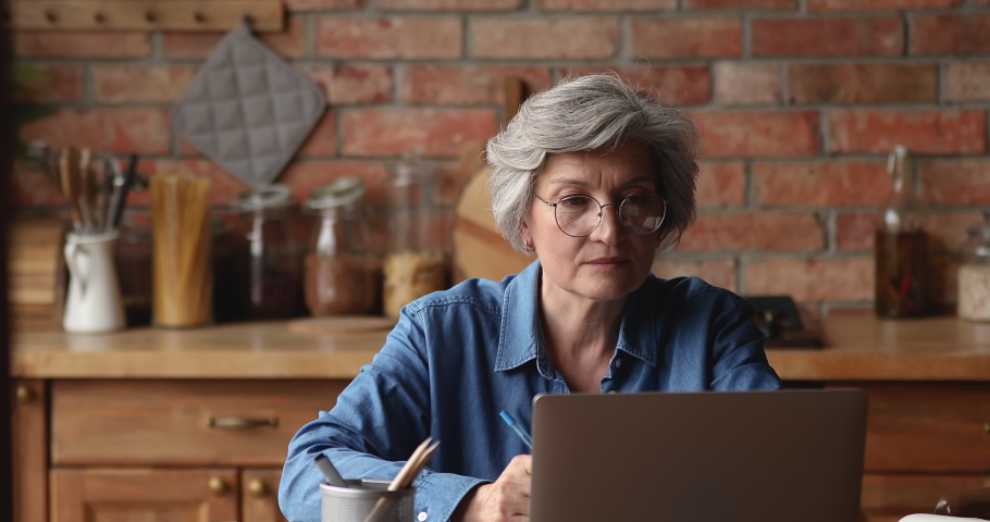 Older woman in glasses use laptop seated in kitchen read good news on-line feels overjoyed, celebrate received great commercial offer, find solution feels happy, e-commerce, betting victory concept Royalty-Free Stock Footage #1066100266