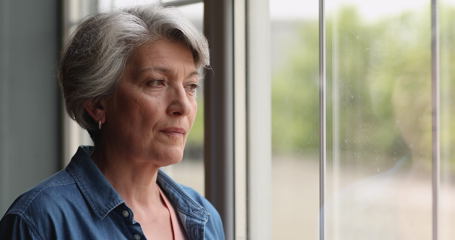 Close up view middle-aged 55s grey-haired thoughtful female standing alone indoor looking out the window. Attractive woman with short hairstyle smiling staring at camera having attractive appearance Royalty-Free Stock Footage #1066100296