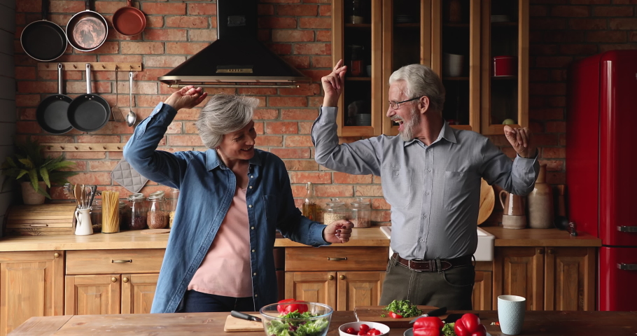 Happy active elderly spouses distracted from vegetable salad preparation dancing in modern cozy kitchen. Aged couple celebrate life event anniversary listening music moving enjoy romantic date concept Royalty-Free Stock Footage #1066102165