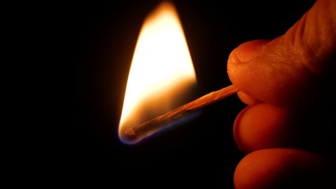 Lighting a match against a matchbox in the dark. Burning match. Matchbox in hand. Flame of fire. Ignition spark. Light a fire. Human hands. Black background. Sulfur is highly flammable.