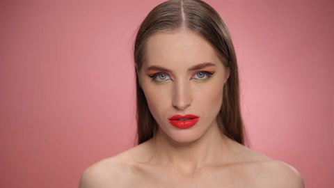A beautiful model with red lipstick on her lips looks at the camera and with her hand smears the lipstick from her lips, turning beauty into mess make up. FHD footage. 