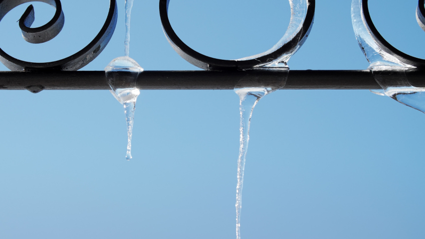 Melting Ice Stalactites on wrought iron. Dripping water. Global warming concept. Blue Sky on background