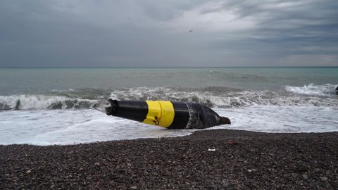A large black and yellow buoy washed ashore after a storm. A broken sea buoy lies on the shore against the backdrop of the sea after a storm.