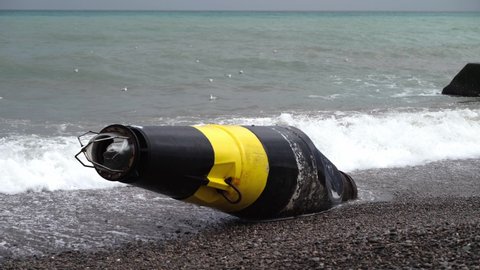 A large black and yellow buoy washed ashore after a storm. A broken sea buoy lies on the shore against the backdrop of the sea after a storm.