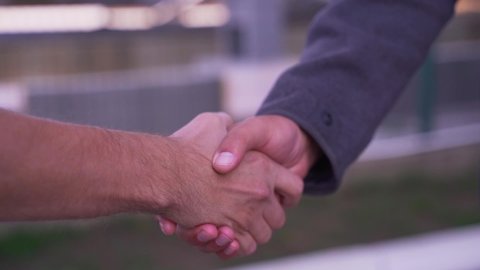 Two men shaking hands greeting each other on the street. Securing a business deal with a handshake.  Close up video shot of men shaking hands. Two colleagues greeting each other with a handshake.