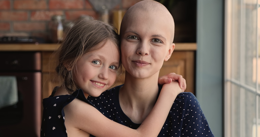 Young bald sick mother cancer patient embrace little daughter in kitchen smile look at camera. Caring kid express tender, gives support, feeling devotion to parent with oncology disease. Love concept Royalty-Free Stock Footage #1066120966
