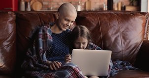 Bald cancer patient mom wrapped herself and daughter with plaid rest on couch spend priceless time together using laptop having fun watch cartoons filled with positive emotions distracted from disease