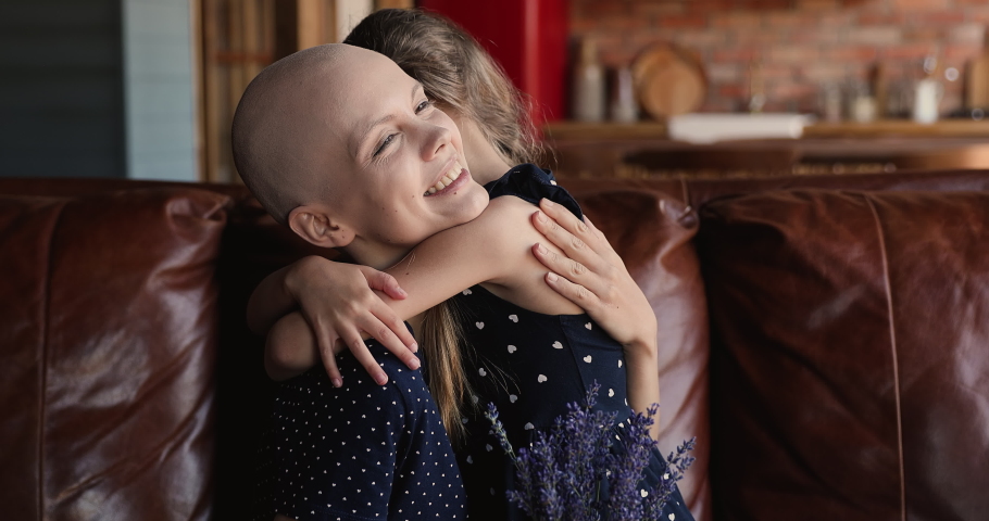 Loving kid make surprise for mother cancer patient, cuddling sit on sofa. Bald woman holds lavender bunch receiving congrats from daughter on oncology disease recovery, celebrate recuperation concept Royalty-Free Stock Footage #1066121197