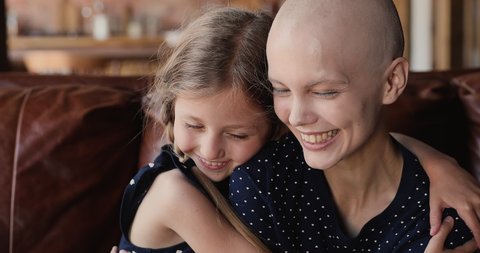 Close up little daughter hugs mother cancer patient. Happy family sit indoor embracing feeling grateful for remission, express love, kid girl supporting mom, encourage her, hoping in recovery concept