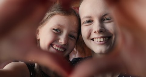 Little adorable girl her young bald mother making heart shape with hands showing symbol of love at camera, close up view happy faces. Share support optimism and hope with other cancer patients concept