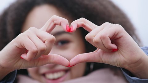 Close-up of female fingers with dark skin and manicure showing shape of heart, Afro American defocused woman demonstrating love affection sympathy symbol makes peace support gesture, focus on hands