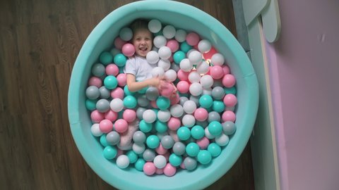 vertical crane shot: little child flounders in round dry pool, mint-colored, fill of multicolored balls, kid laughs, throws balls at up to camera, while shooting used lens-probe 24mm