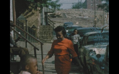 1960s: Women and children walk along city sidewalks. Girl leans from apartment window and speaks. People sit on stoops and walk on sidewalk. Man shuts trunk of car.