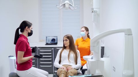 A young female dentist talks to a patient before starting treatment or a procedure at a modern dental clinic. a specialist doctor with an assistant explains, advises, consultation woman in office 