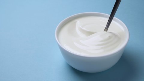 Bowl of fresh greek yogurt on blue background, sour cream with spoon
