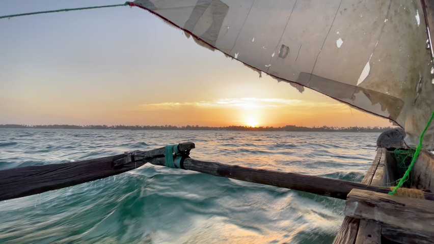 Old traditional maritime traditional vessel Dhow boat sailing under torned sail in the open Indian ocean near Zanzibar island in beautiful sunset time, Tanzania. Traveling 4K footage concept.