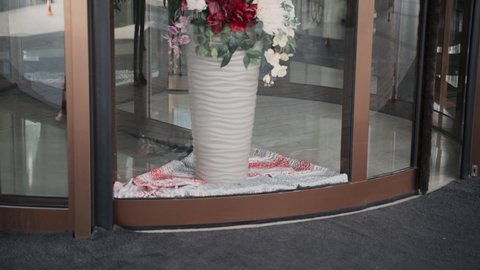 Close-up, glass transparent revolving door, vases with artificial flowers stand on a towel